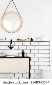 Round mirror above white cabinet in simple bathroom interior. Real photo
