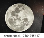 A round moon with a greyish color is shown in the image. The moon is placed on a black surface, which could be a countertop or a table