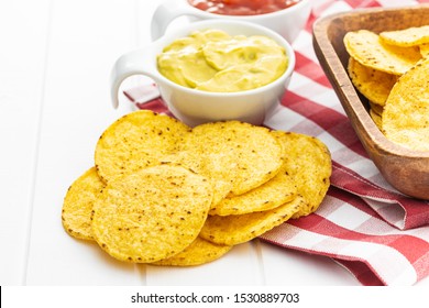 Round nacho chips and avocado dip. Yellow tortilla chips and guacamole in bowl on white table.
