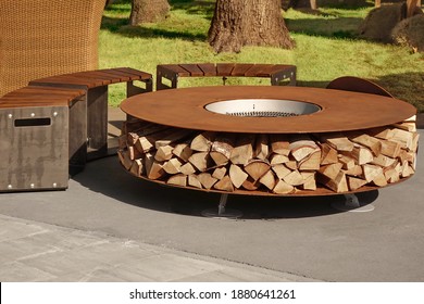 Round Patio Iron Fire Pit Table For Outdoor Leisure Party. Steel Rounded Fire Pit With Grill Top On Backyard Party Place. Grill Appliance And Fireplace On The Back Yard Lawn.