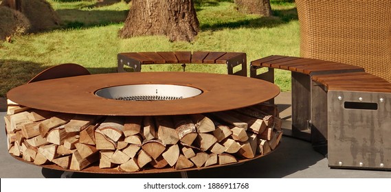 Round Patio Iron Fire Pit Table For Outdoor Leisure Party. Steel Rounded Fire Pit With Grill Top On Backyard Party Place. Grill Appliance And Fireplace On The Back Yard Lawn.