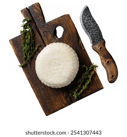 A round piece of white cheese rests on a rustic wooden cutting board, accompanied by a knife and sprigs of fresh thyme on a white background. - Powered by Shutterstock