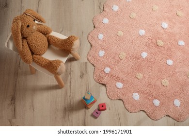 Round pink rug with polka dot pattern and toys on wooden floor in baby's room, above view
