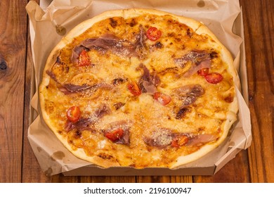 Round Pizza With Ham And Cherry Tomatoes Served In Open Cardboard Pizza Box On The Old Rustic Table
