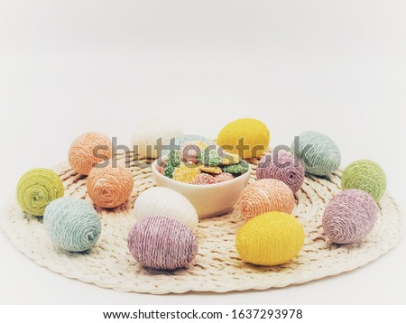 Round placemat topped with Easter eggs covered in sparkly string and a white bowl of pastel colored white chocolate mint candies.