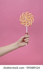 Round Rainbow Lolipop In Hand On Pink Background