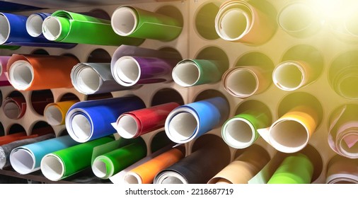 Round rolls with self-adhesive vinyl film in production. Printing warehouse. Multicolored film is laid out on the shelves. Color selection for advertising design.Pasting a car with a film.