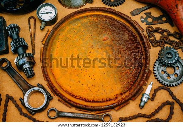 Round rusty board for logo, label or\
information in the center of rusty tools, gears on vintage\
background. Motorcycle equipment and repair template. Top\
view