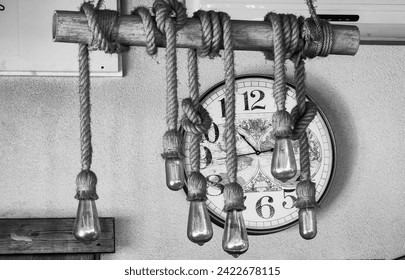 Round shape clock wall, background. Framed by lightbulbs hanging on the rope. Black white, monochrome.