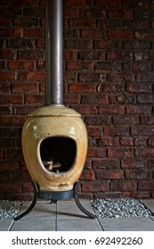 A Round Shape Small Pot Belly Stove With A Rustic Brick Wall In The Background.