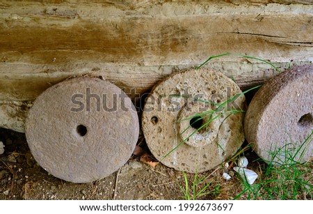 Round shape stone for wheat bran milling standing in village house in front of the wooden wallBricks wall made of mud in village house textured wall.