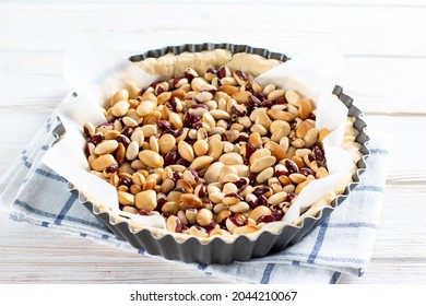 Round shortcrust pastry case with beans ready for blind baking. Beans used as pastry weights in an uncooked pie crust lined with greaseproof paper - Shutterstock ID 2044210067