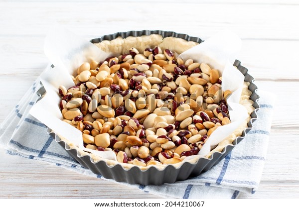 Round shortcrust pastry case with beans\
ready for blind baking. Beans used as pastry weights in an uncooked\
pie crust lined with greaseproof\
paper