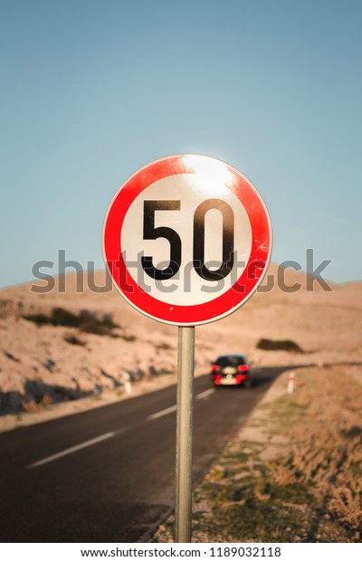 Round speed limit road sign (50 km per hour) on the\
road behind the village in Croatian Island with hills and car on\
background. Country road with a fifty kilometres speed limit\
traffic sign.
