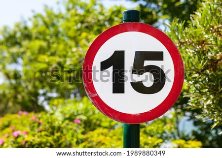 Round speed limit sign fifteen on the background of trees.