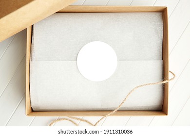 Round sticker mockup, circle white adhesive label in brown gift box.