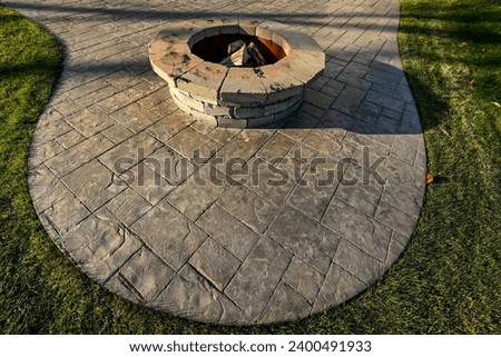 round stone fire pit on stamped concrete patio in grass yard

