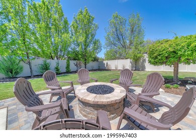 A Round Stone Table With Plastic Chairs In Front Of The House