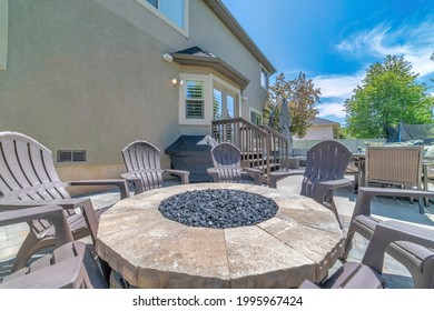 A Round Stone Table With Plastic Chairs In Front Of The House