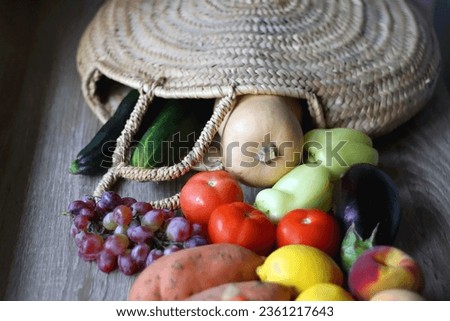 Round straw bag with seasonal fruit and vegetable on wooden background. Late summer or early autumn. Selective focus.