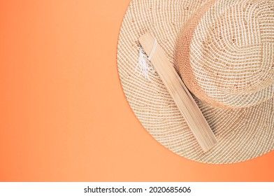 A Round Straw Hat And A Folding Hand Fan Isolated On A Peach Background With Free Space For Text- Concept For Hot Summer Weather