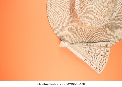 A Round Straw Hat And A Folding Hand Fan Isolated On A Peach Background With Free Space For Text- Concept For Hot Summer Weather