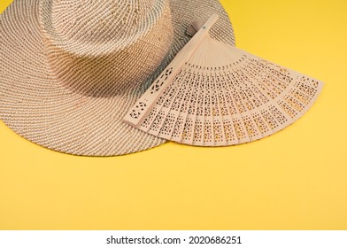 A Round Straw Hat And A Hand Fan Isolated On A Yellow Background With Free Space For Text- Concept For Hot Summer Weather