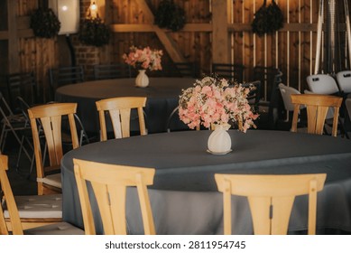 Round table adorned with a gray tablecloth and floral arrangement in a rustic wooden setting, featuring wooden chairs and decorative greenery in the background