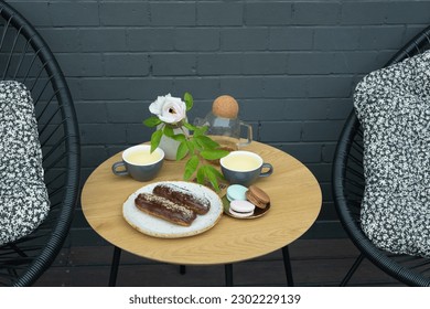 Round table in a cafe with two cups of tea with eclairs and macarons. Sweet food still life.
