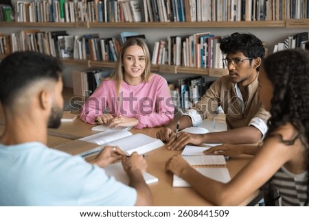 Round table peer learning. Successful group of 4 diverse multicultural students pupils engaged in scientific conversation at campus library study together using paper notes books to discuss assignment