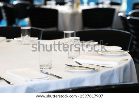 A round table with a white tablecloth at a large function centre, set up, ready with plates, glasses and cutlery for guests. Formal event catering and function hire. 