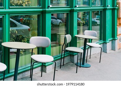 A Round Tables With Soft Grey Chairs In A Street Cafe Waiting For Visitors. Old Town. Green Stylish Facade. Restaurant. Dining. Empty. No People. Outside. Outdoor