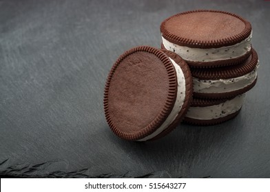 Round Vanilla And Cookie Ice Cream Sandwich Bar Leaning Against A Stack Of Three Ice Cream Sandwiches With Copy Space