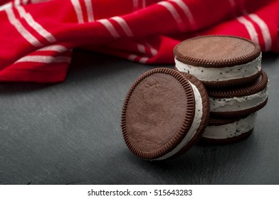 Round Vanilla And Cookie Ice Cream Sandwich Bar Leaning Against A Stack Of Three Ice Cream Sandwiches With Copy Space And A Red Kitchen Towel