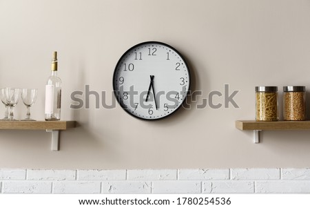 Round wall clock between wooden kitchen shelves