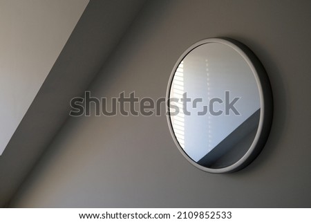 Round wall mirror reflections in a light grey room with angled dormer cornice. Sylish elegant and sophisticated. Simple enigmatic monochrome minimalist abstract interior design element. 