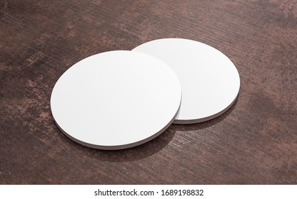 Round white blank drink coasters lying on the wooden table. Mock Up. Circular beer mat to protect the surface of a table.