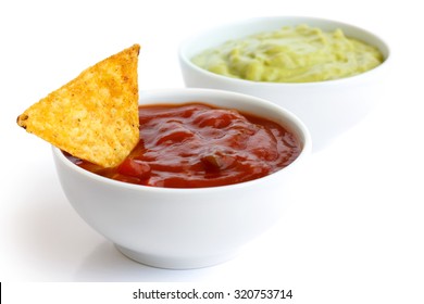 Round White Bowl Of Tomato Salsa Dip Isolated In Perspective. Tortilla Chip In Dip. Bowl Of Guacamole In Background.