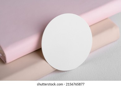 Round White Gift Tag Mockup On Beige And Pink Book Background. Blank Paper Circular Price Sticker Tag Mockup, Sale And Black Friday Concept, Element For Design, Label Mockup