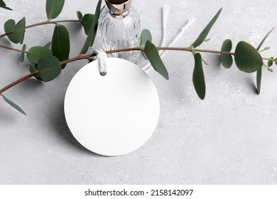 Round white gift tag mockup with eucalyptus leaves on grey background, label tag mockup, Wedding favor tag for souvenir, sign for greeting message close up, element for design