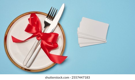 Round white plate and tied with red bow view with knife on blue background, festive table setting, top view - Powered by Shutterstock