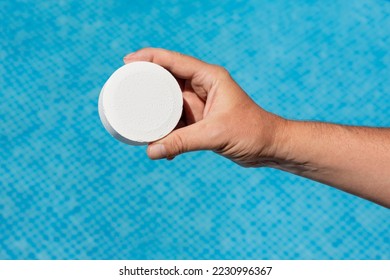 Round white pool chlorine tablet to prevent the appearance of fungi and bacteria. Hand holding pool chlorine tablet over blue water. Large chlorine tablet for floating dispenser - Powered by Shutterstock