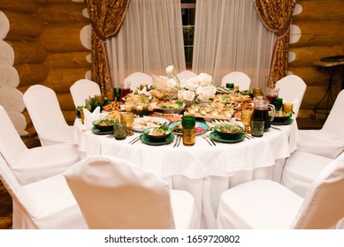 The round white table is filled with a large amount of food and various snacks in a luxurious interior, beautiful serving of the holiday table