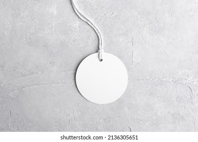 Round White Tag Mockup With White Cord, Close Up. Blank Paper Price Tag Isolated On Grey Stone Background With Copy Space.