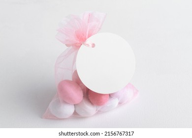 Round White Tag Mockup With Gift With Pink Chocolate Confetti In A Bag With Pink Ribbon. Wedding Favor Tag For Souvenir O Gift For Gues, Sign For Message Greeting, Close Up, Element For Design