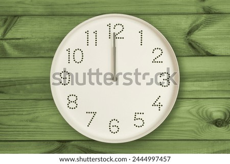 Round white wall clock at 12 o'clock on green wood background. Concept of daily regime, lunch time, Daily Grind, Noon Break