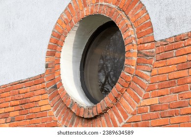 Round window. Red brick wall and light plaster.