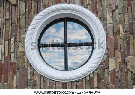 the round window reflects the sky and clouds. in the stone wall on the facade