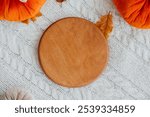 A round wooden board placed on a cozy knitted fabric surrounded by autumn decor.