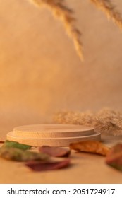 Round Wooden Podium For Food Or Cosmetics On Warm Yellow Kraft Paper Background. Plate For Perfume With Dried Flowers And Apple Leaves In The Front Plane. Mockup For Product Presentation